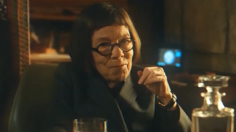 Linda Hunt, seated, makes a hand gesture with a smirk on her face.