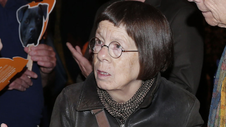 Linda Hunt, dressed in a leather outfit, gazes away from the camera.