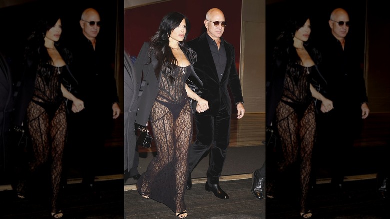 Sporting a sheer black dress that shows her underwear, Lauren Sánchez holds hands with Jeff Bezos while walking.