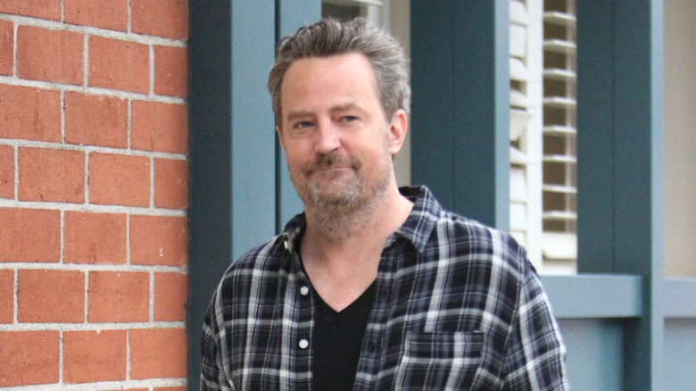 Matthew Perry walking down the street wearing a plaid shirt