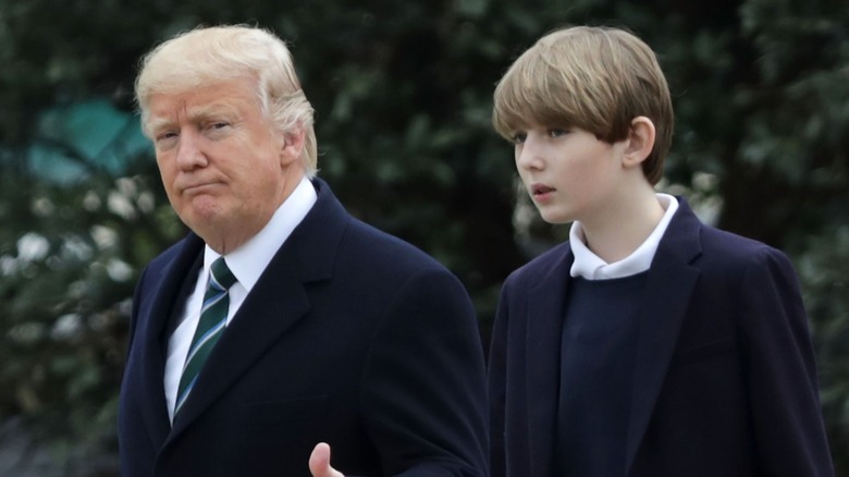 Sporting bangs and a navy blue suit-sweater combo, Barron Trump walks alongside his dad, Donald Trump.