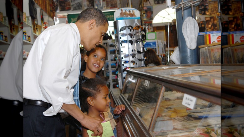 Malia and Sasha Obama smiling with Barack Obama at a general store