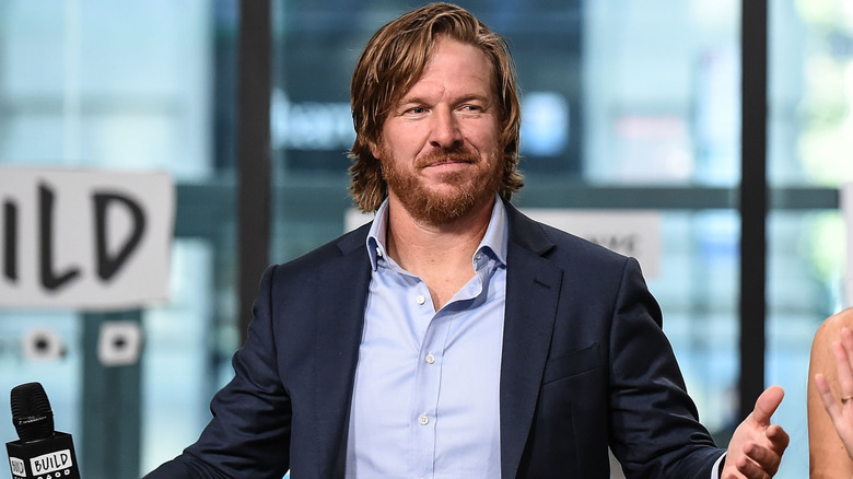 Chip Gaines shrugs animatedly while speaking on stage.