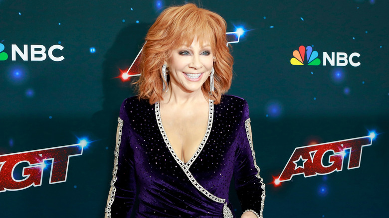 Reba McEntire posing in a purple outfit with a big smile