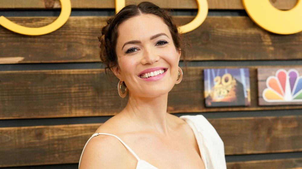 Mandy Moore in a white outfit, smiling with her hair pulled back at a This Is Us-themed event