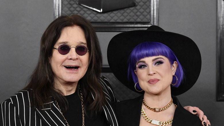 Ozzy and Kelly Osbourne smiling and embracing while posing together at the Grammys