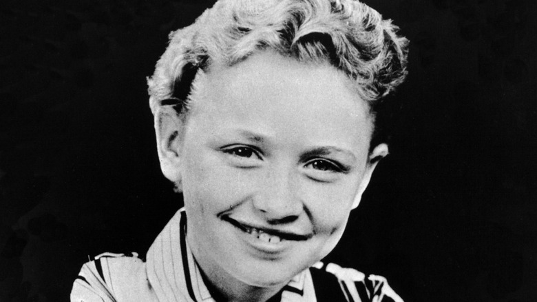 A young Dolly Parton, wearing a striped shirt, smiles.