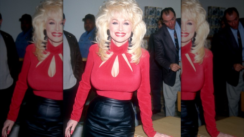 Dolly Parton, dazzling in a red-and-black outfit, gives a big smile.