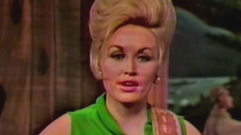 Dolly Parton, wearing a green dress, sings while gazing into the camera.