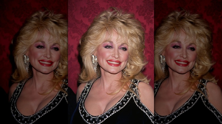 Dolly Parton, wearing a revealing outfit, smiles while looking away from the camera.