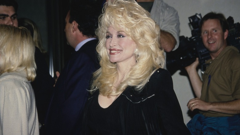 Dolly Parton, wearing a black fringed outfit, breaks into a huge grin.