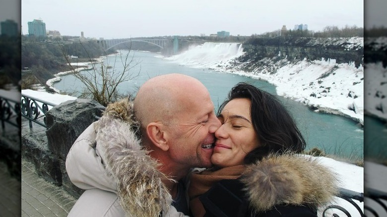 Bruce Willis and Emma Heming Willis smiling with faces pressed together on a bridge