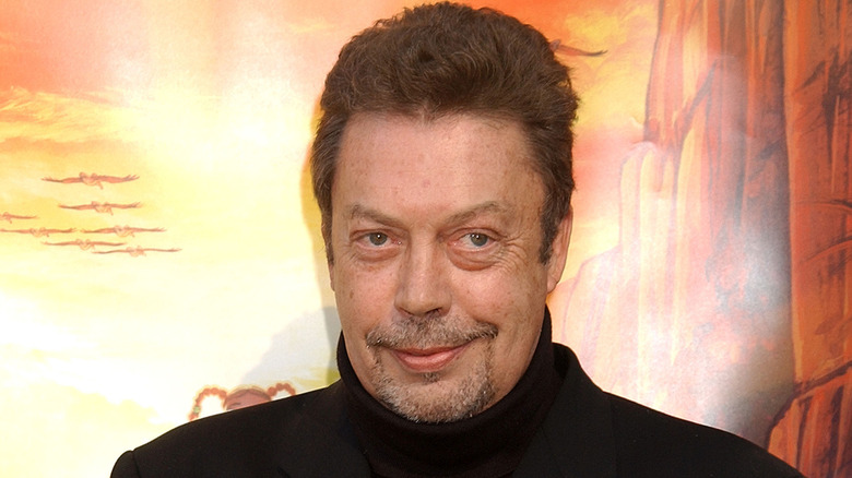 Tim Curry smiling in a black turtleneck.