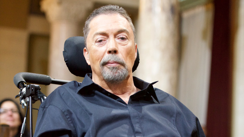 Tim Curry wearing a dark collared shirt.