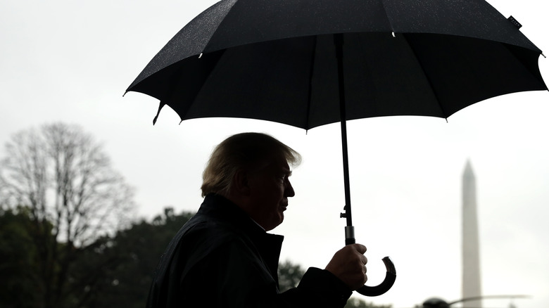 Donald Trump holds an umbrella and talks to reporters before leaving the White House October 15, 2018 in Washington, DC.