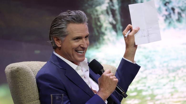 Gavin Newsom laughs as he holds up a document.