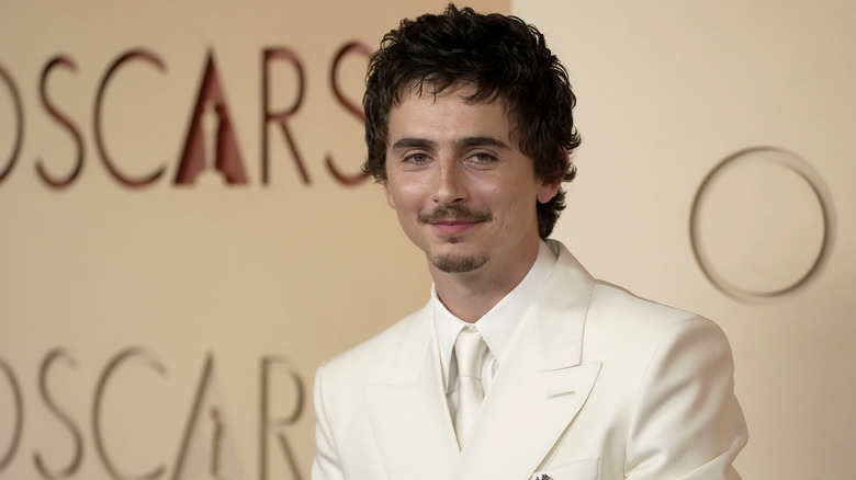 Timothee Chalamet poses at 2026 Oscars in a white suit and tie.