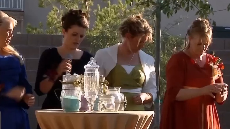 The stars of "Sister Wives," wearing different outfits, stand behind a display of jars.