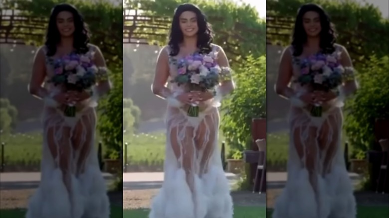 Alliya de Batista, wearing a see-through wedding gown, walks down the aisle carrying a bouquet of flowers.