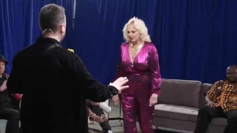 Angela Deem, wearing a long-sleeved pink jumpsuit, walks toward a "90 Day Fiancé" crew member.