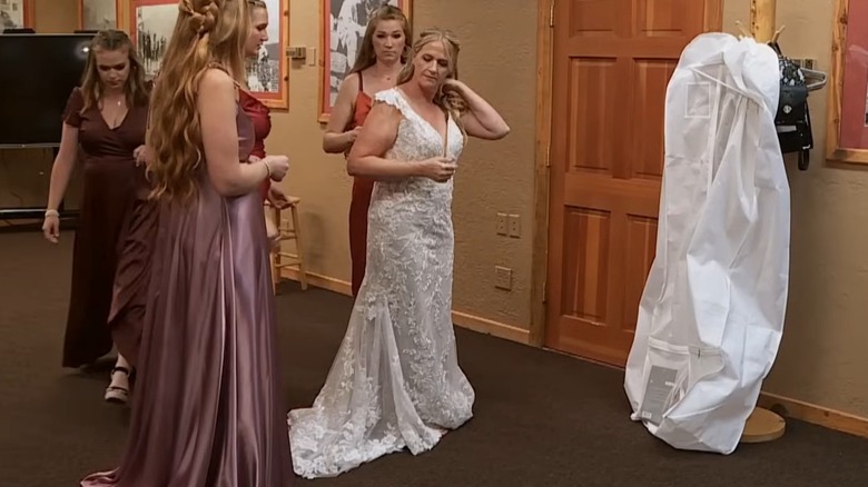 Christine Brown, wearing a lacy wedding gown, adjusts her hair as other "Sister Wives" cast members look on.
