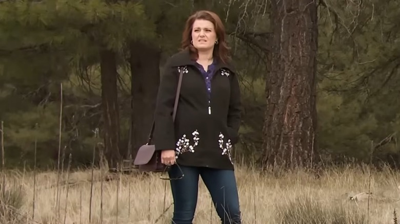 Robyn Brown, wearing a pair of jeans and a coat, looks sideways while standing on a grassy field.