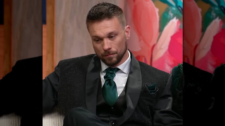 Matt Jlassi, sporting a green ruched tie, looks to the side with a gentle smile.