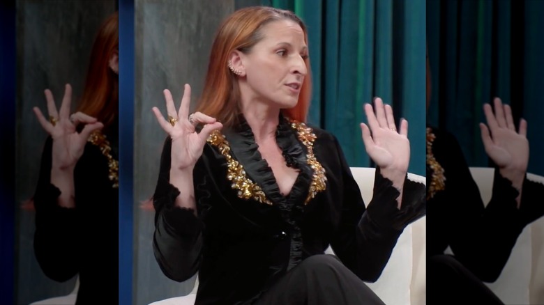 Kris Foster, wearing a black and gold outfit, raises her eyebrows while speaking.