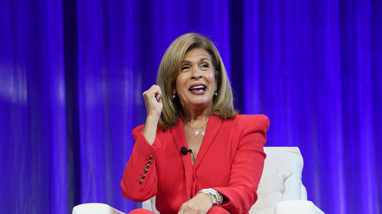 Hoda Kotb gesturing onstage in a red suit against a blue background