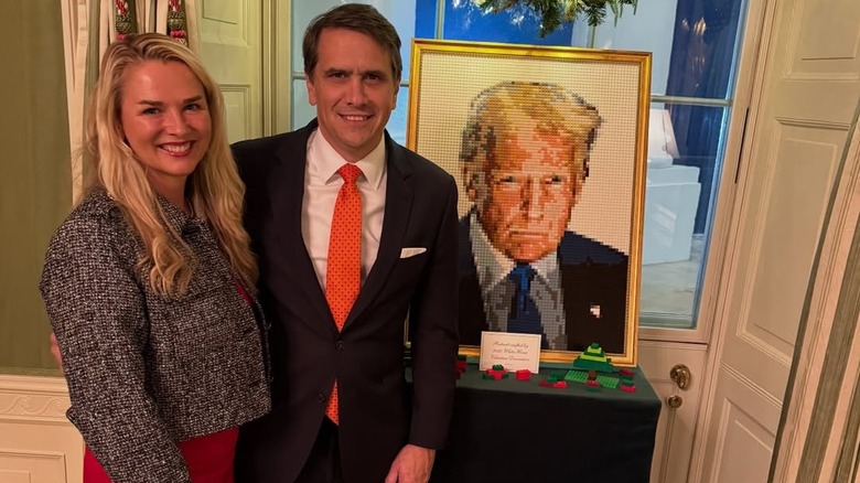 Todd Blanche and wife Kristine Blanche posing in front of a portrait of Donald Trump.