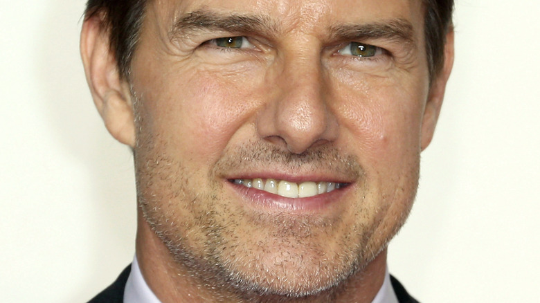 Tom Cruise smiles in front of a white background