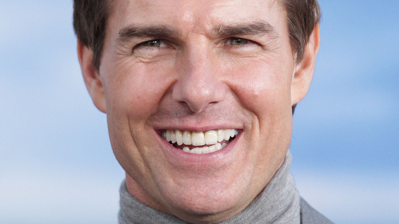 Tom Cruise smiles in a light gray turtleneck