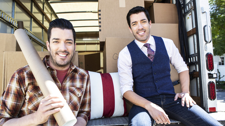 The Property Brothers, Drew and Jonathan Scott, smile in a moving truckbed