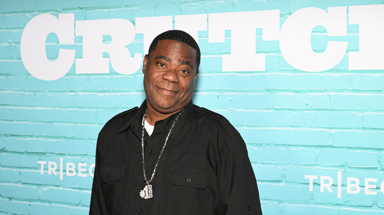 Tracy Morgan smiling while posing at an event in a black shirt and a silver chain