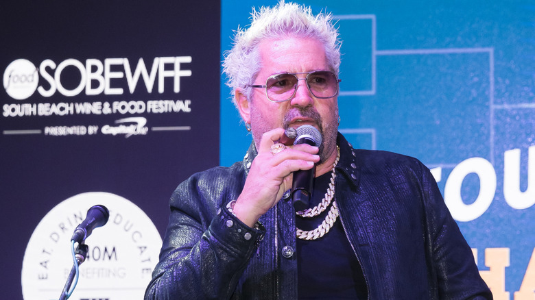 Guy Fieri on stage holding a microphone and cigar