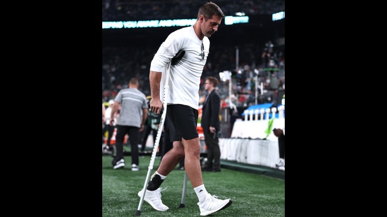 Aaron Rodgers using crutches wearing a white long-sleeved t-shirt