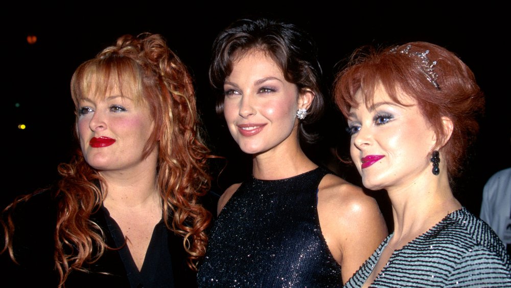 Wynonna Judd, Ashley Judd, Naomi Judd standing together with small smiles at a movie premiere