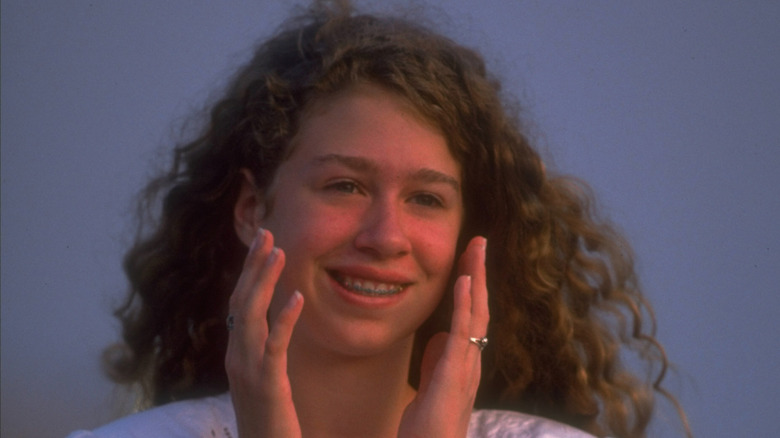 Teenage Chelsea Clinton smiling while holding her hands to face