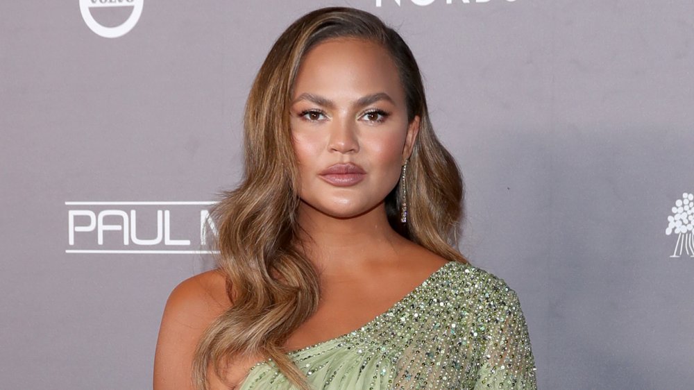 Chrissy Teigen posing in a bejeweled dress with a neutral expression