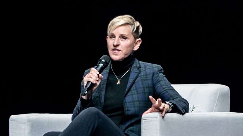 Ellen DeGeneres in a blue plaid suit, sitting down and speaking into a mic