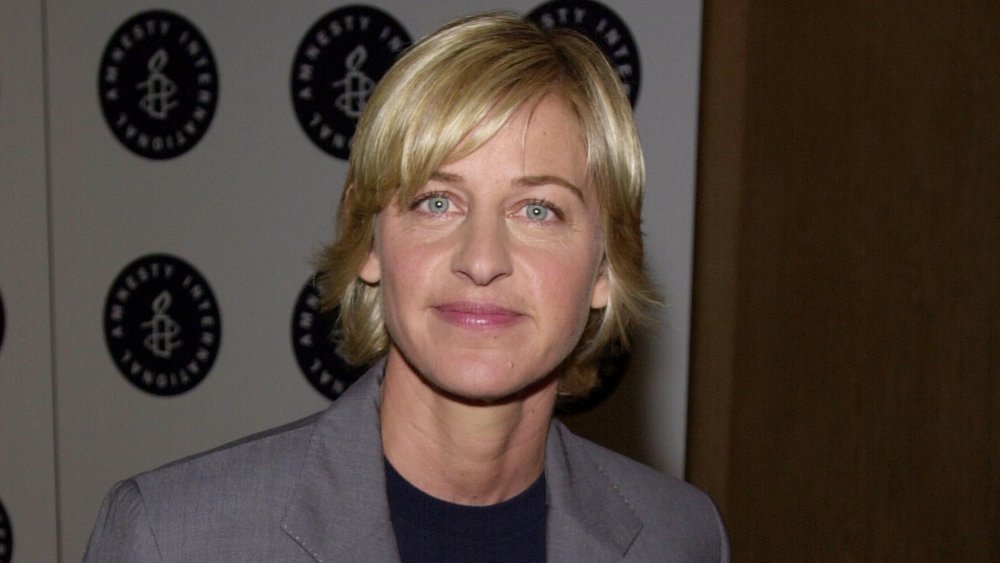 Ellen DeGeneres in a grey suit and blue t-shirt, posing with a small smile