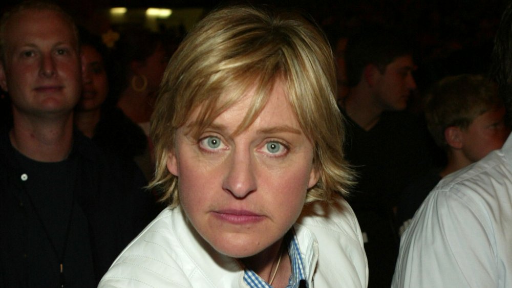Ellen DeGeneres in a blue plaid shirt and white jacket, looking straight into the camera with a neutral expression