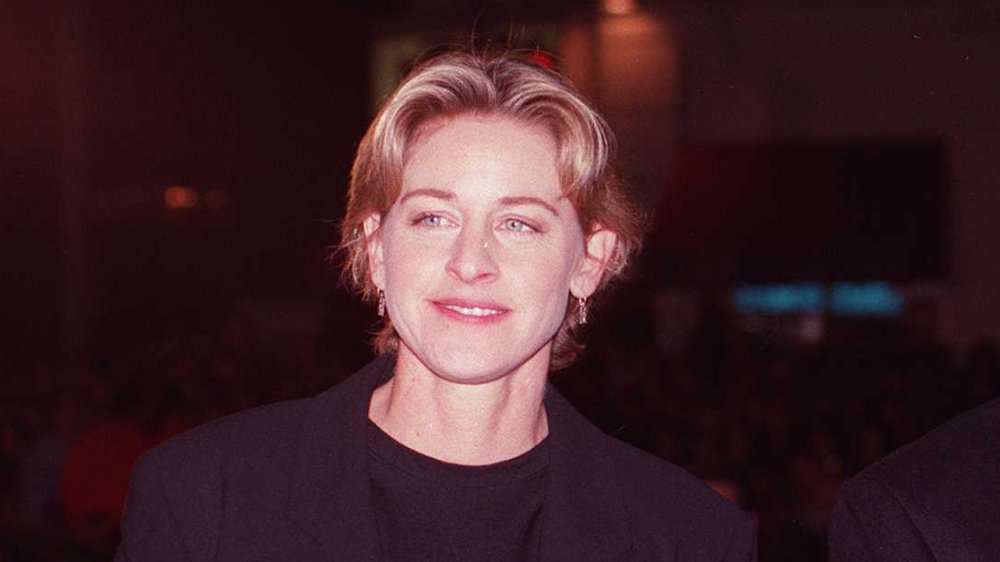 Ellen DeGeneres in a black suit, posing with a small smile in the early '90s