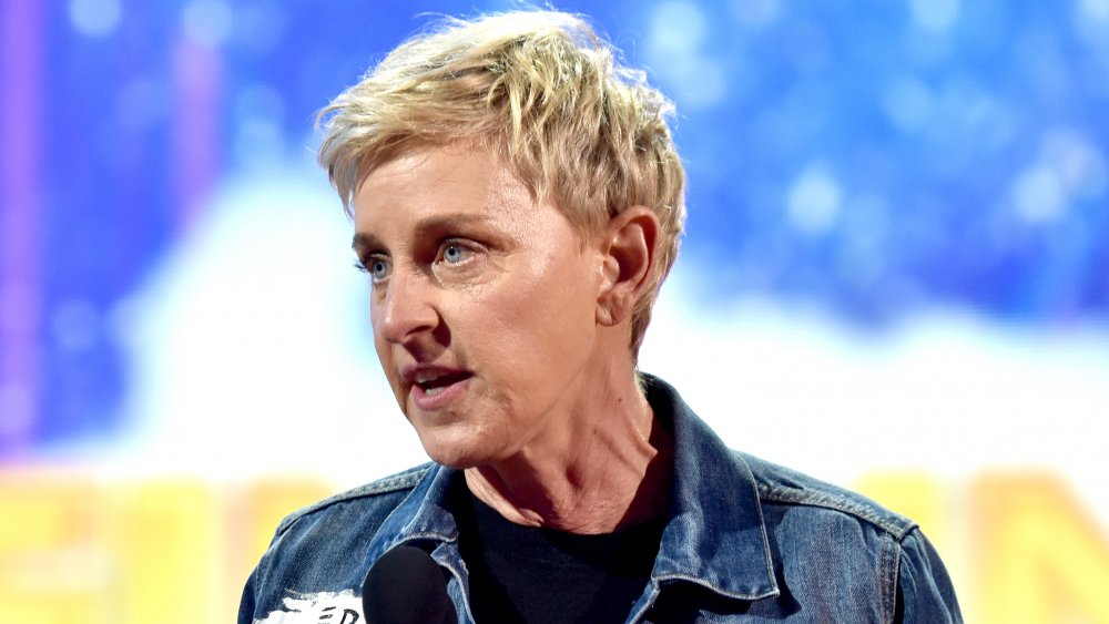Ellen DeGeneres in a jean jacket, speaking into a mic with an intense expression