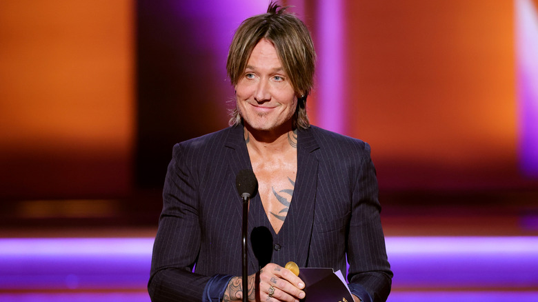 Keith Urban smiling and holding an envelope on stage