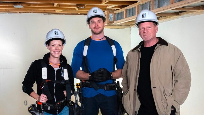 Sherry Holmes, Mike Holmes Jr., and Mike Holmes posing together with construction hats on