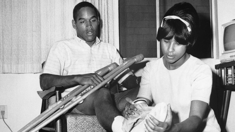 O.J. Simpson sitting with crutches while a woman tends to his foot