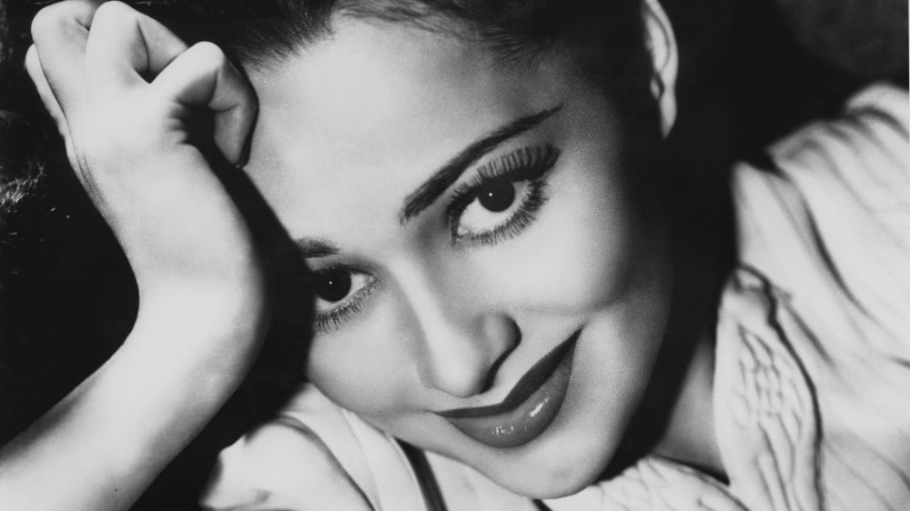 Olivia de Havilland looking straight at the camera with a smile, leaning her head against her hand