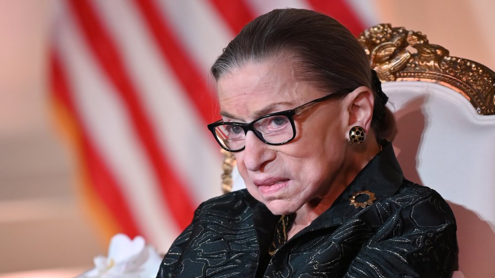 Ruth Bader Ginsburg seated, gold earrings and black glasses