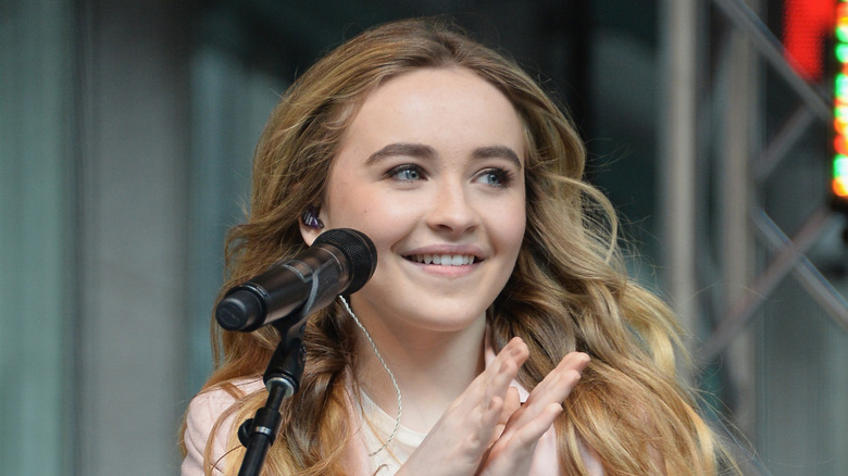 Young Sabrina Carpenter smiling and clapping on stage
